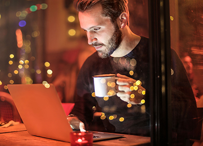 Man holding mug while working on laptop at coffee shop